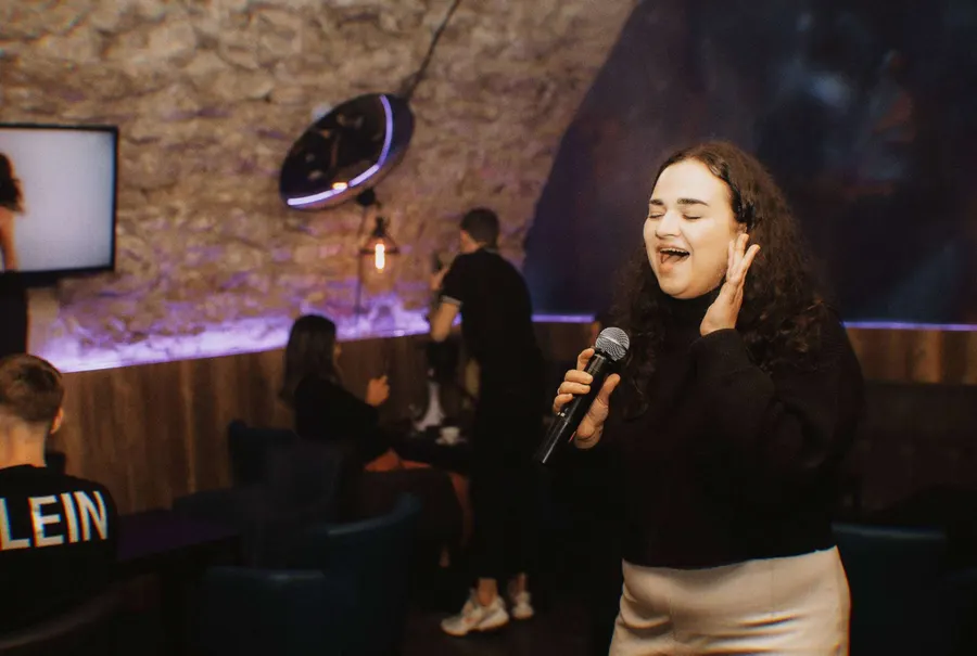 A guest singing joyfully into a microphone under purple lighting
